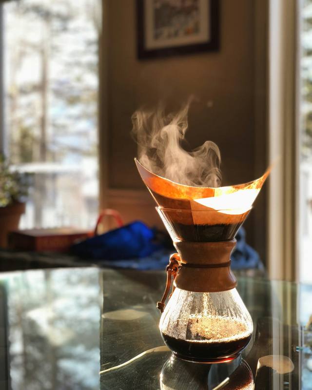 Steaming pour-over brewer on a glass table in morning light